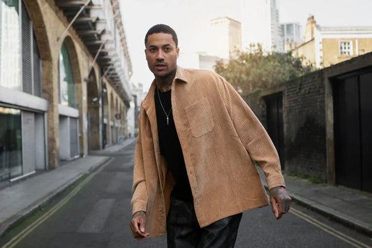 Man wearing a tan overshirt jacket walking on a quiet city street.